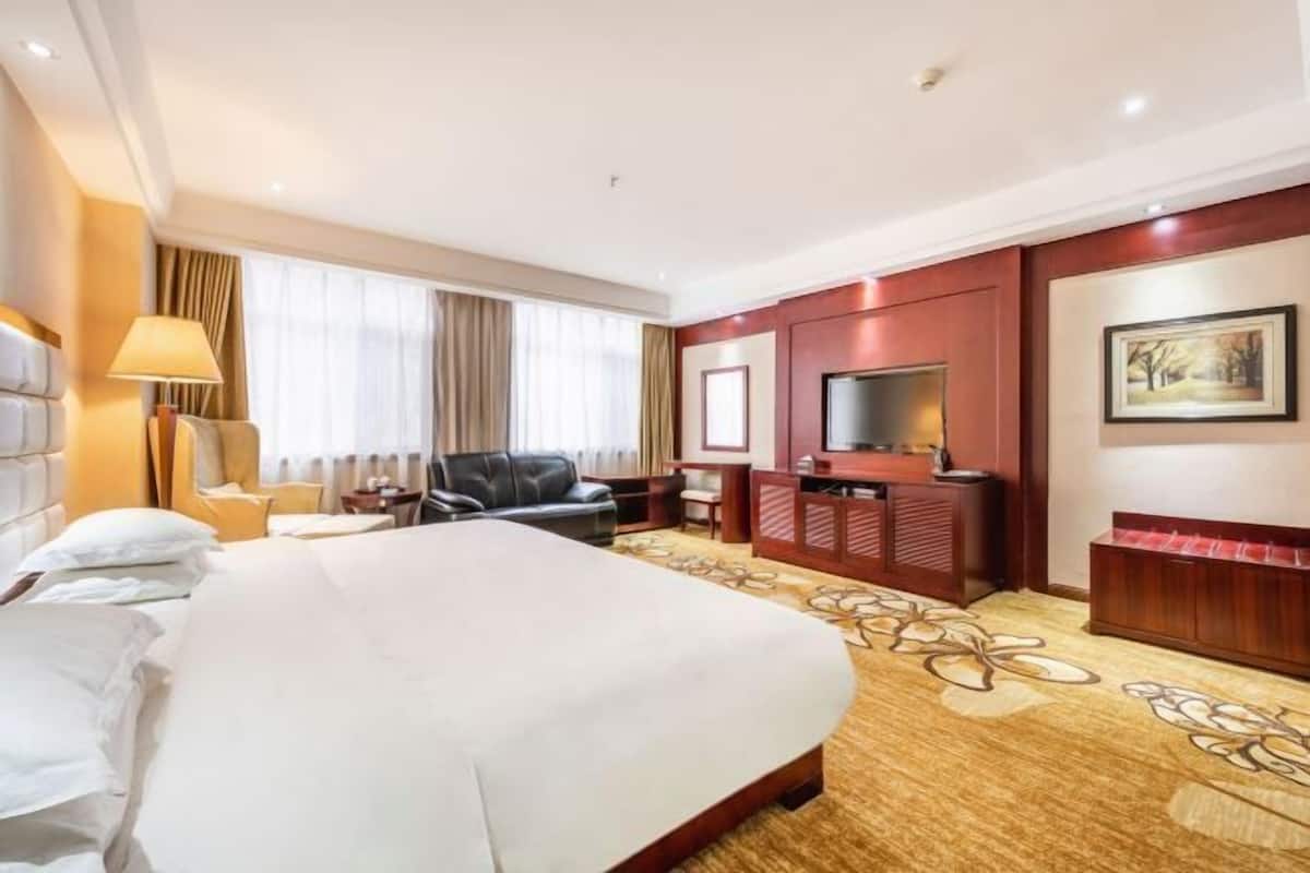 A hotel room with a large bed, a desk, a chair, a TV, and a painting on the wall.