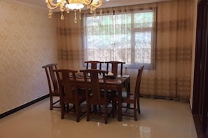 A dining area with a table and chairs, a chandelier, and a window with curtains. - Longhai Hotel (Tanchang)