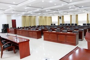 A conference room with multiple rows of chairs, a large wooden desk, and a podium. - Longhai Hotel (Tanchang)
