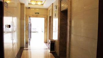 Pasillo de hotel con suelo reflectante, una puerta con la etiqueta 'EXIT' y una lámpara empotrada en la pared.