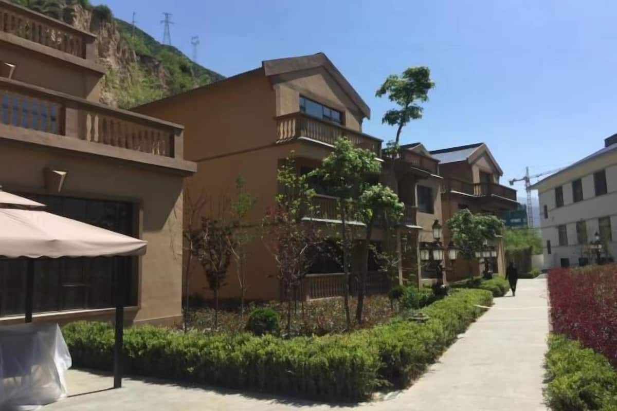 A residential building with balconies, a covered outdoor seating area, and a pathway lined with greenery.