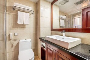 A bathroom with a white toilet, a sink with a mirror above it, and a towel rack with folded towels. - Longhai Hotel (Tanchang)