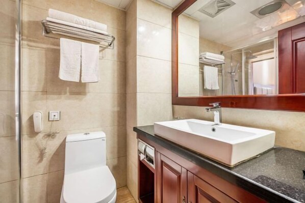 Un baño con inodoro blanco, lavabo con espejo y toallero con toallas dobladas.
