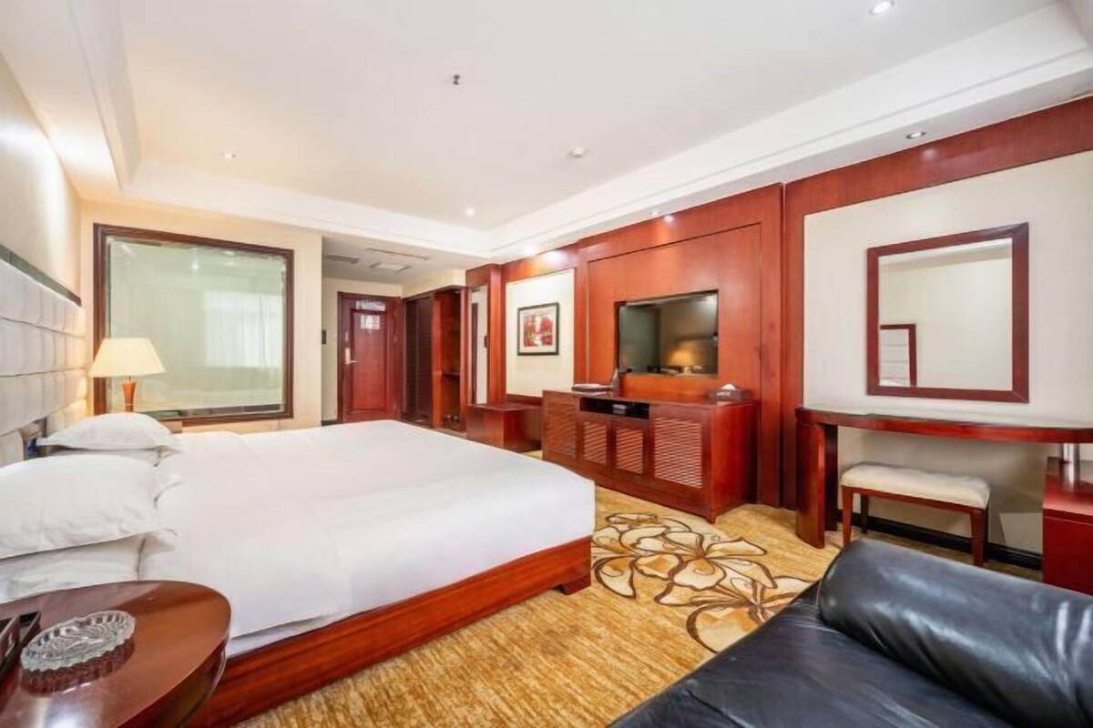 A hotel room with a bed, a desk, a chair, a TV, and a large window.