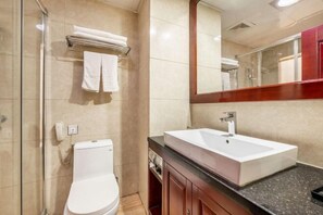 Un baño con inodoro blanco, lavamanos con espejo y un perchero con dos toallas.
