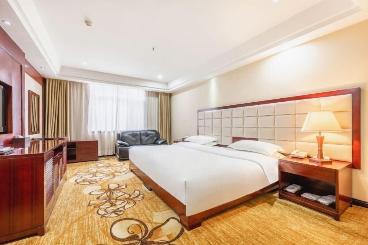 Habitación de hotel con una cama grande, un escritorio, una silla, un televisor y una ventana con cortinas.