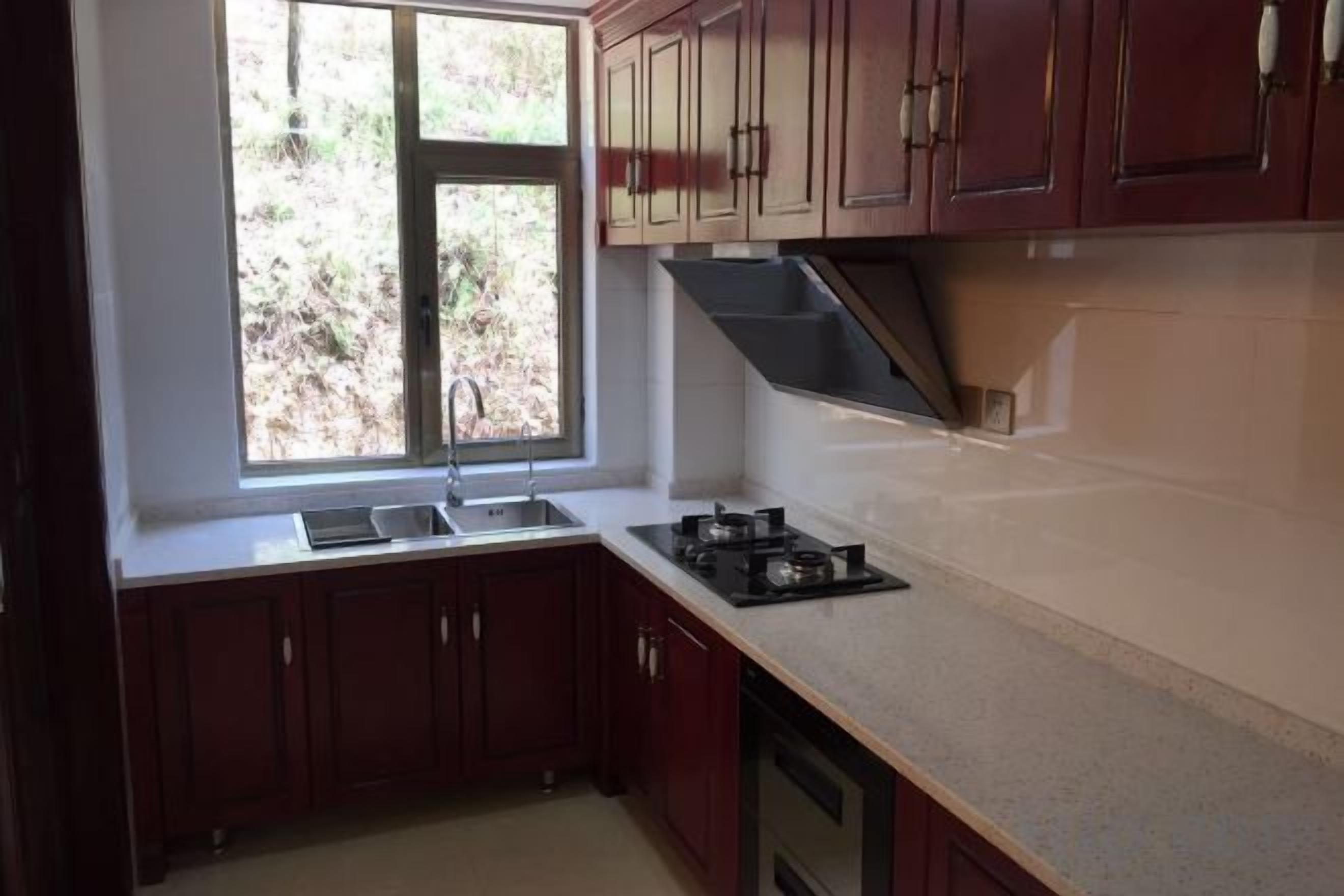 A kitchen with a window, dark wooden cabinets, a countertop, and a stove.