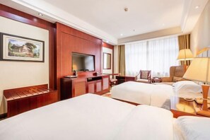 Habitación de hotel con dos camas, televisión, escritorio y una silla.
