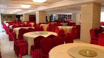 A banquet hall with round tables and red chairs, a chandelier, and a television screen.