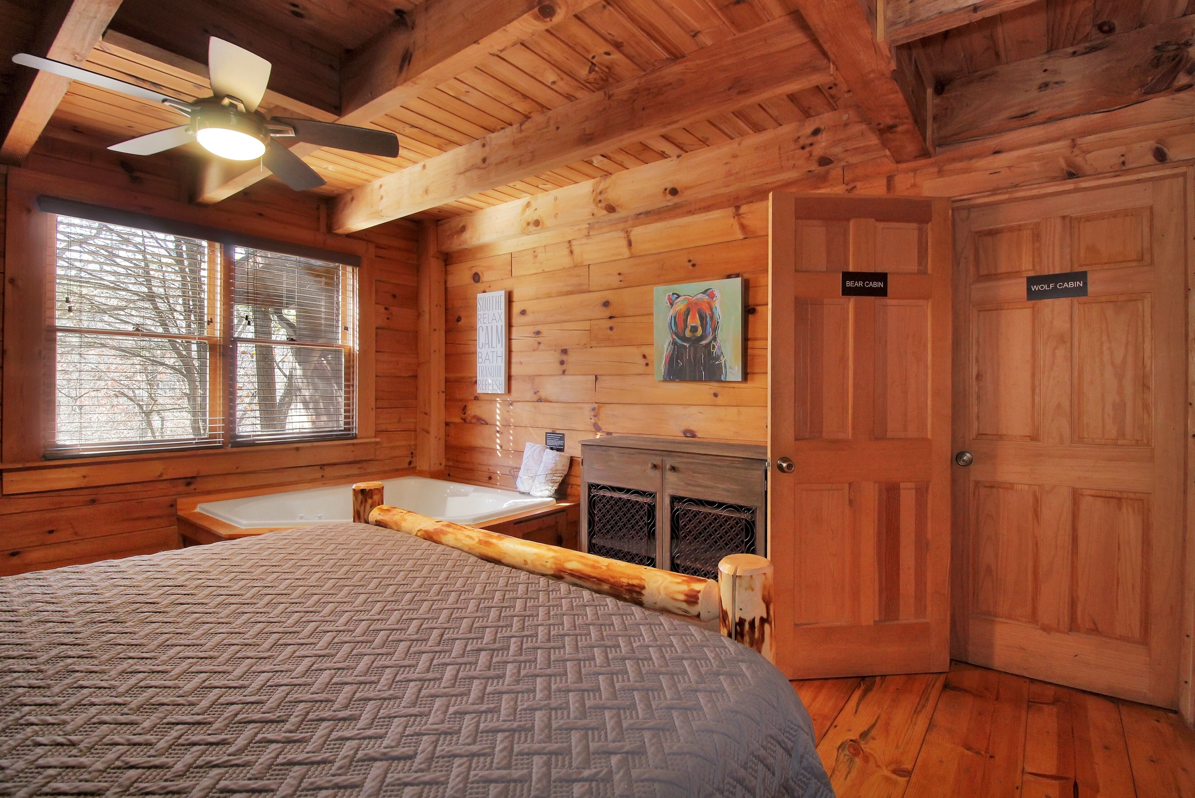A cabin with a bed, a window with blinds, a painting, and a sign indicating 'BEAR CABIN'.