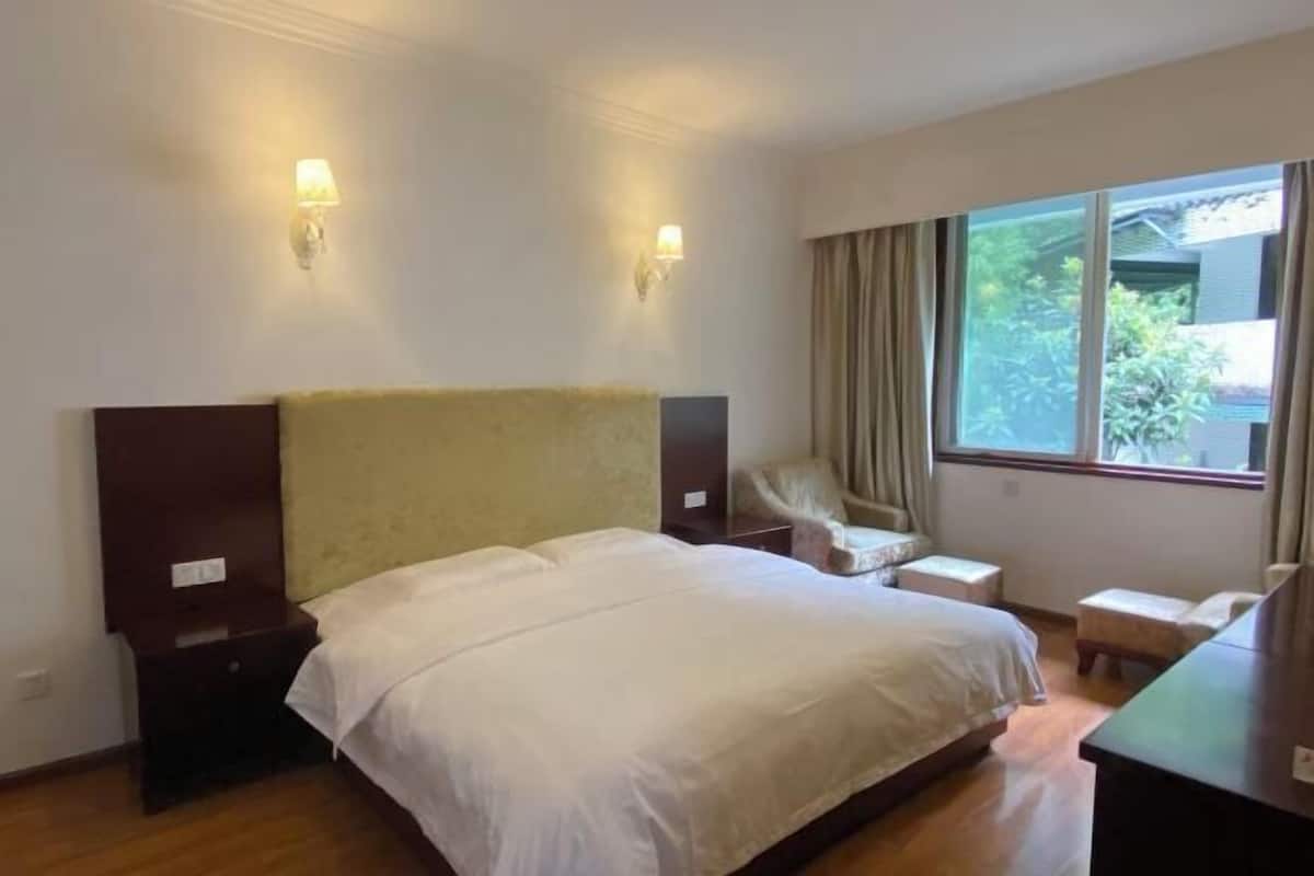 A hotel room with a large bed, two bedside lamps, a small desk, a chair, and a window with curtains.
