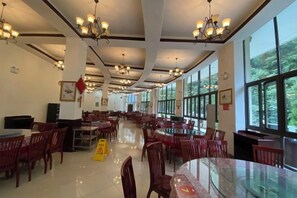 Un'ampia sala da pranzo con diversi tavoli e sedie, grandi finestre e lampadari a soffitto.