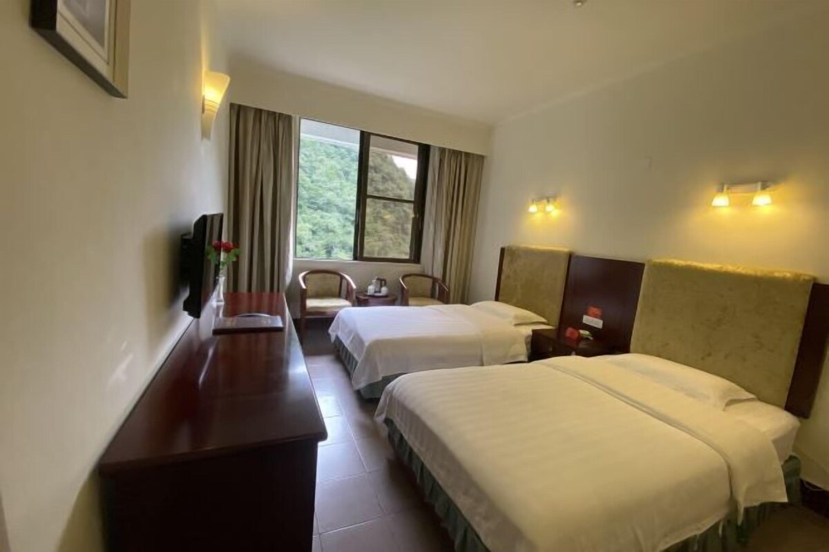 A hotel room with two beds, a desk, a chair, and a window with curtains.