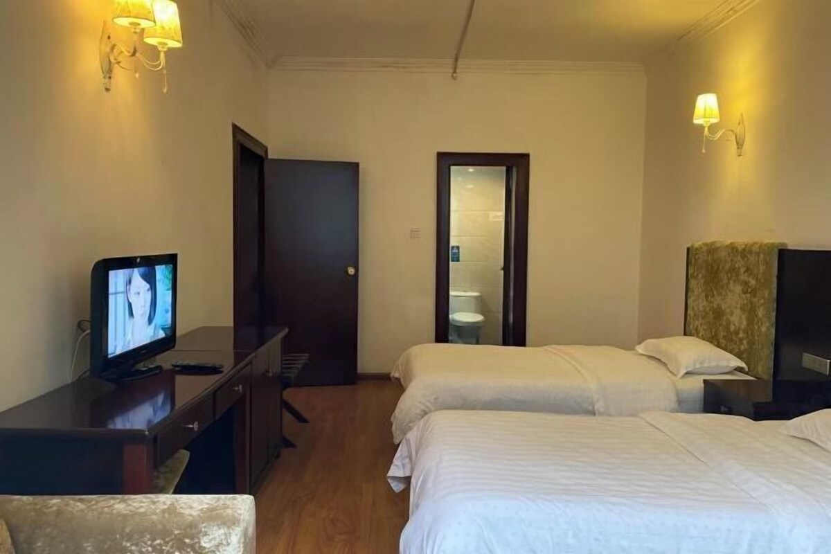 A hotel room with two beds, a desk with a television, and a door leading to a bathroom.