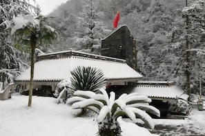 A traditional building with a snow-covered roof and a red flag, surrounded by snow-laden trees.