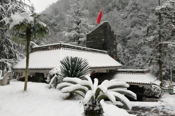 A traditional building with a snow-covered roof and a red flag, surrounded by snow-laden trees. - Xiling Shanzhuang Hotel (Dayi)