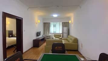 A hotel room with a green pool table, a sofa, a television, and a window with curtains.