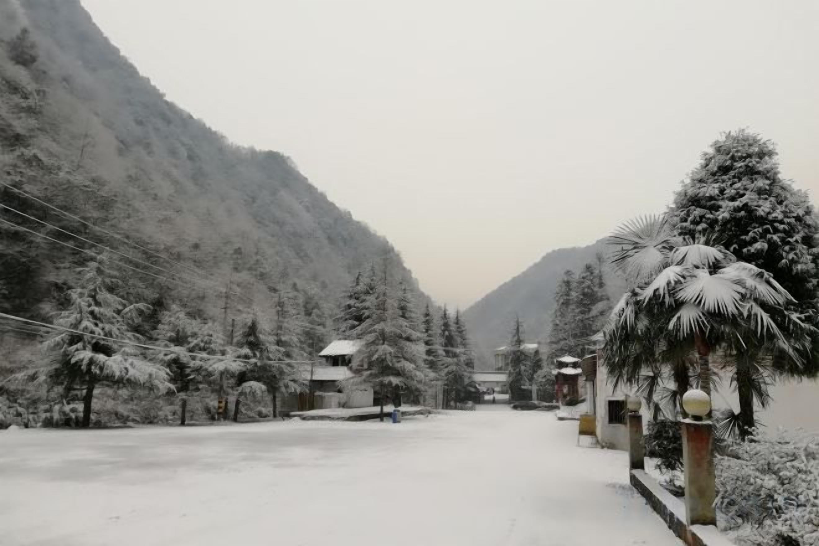A snow-covered mountain road with buildings and trees along the sides.