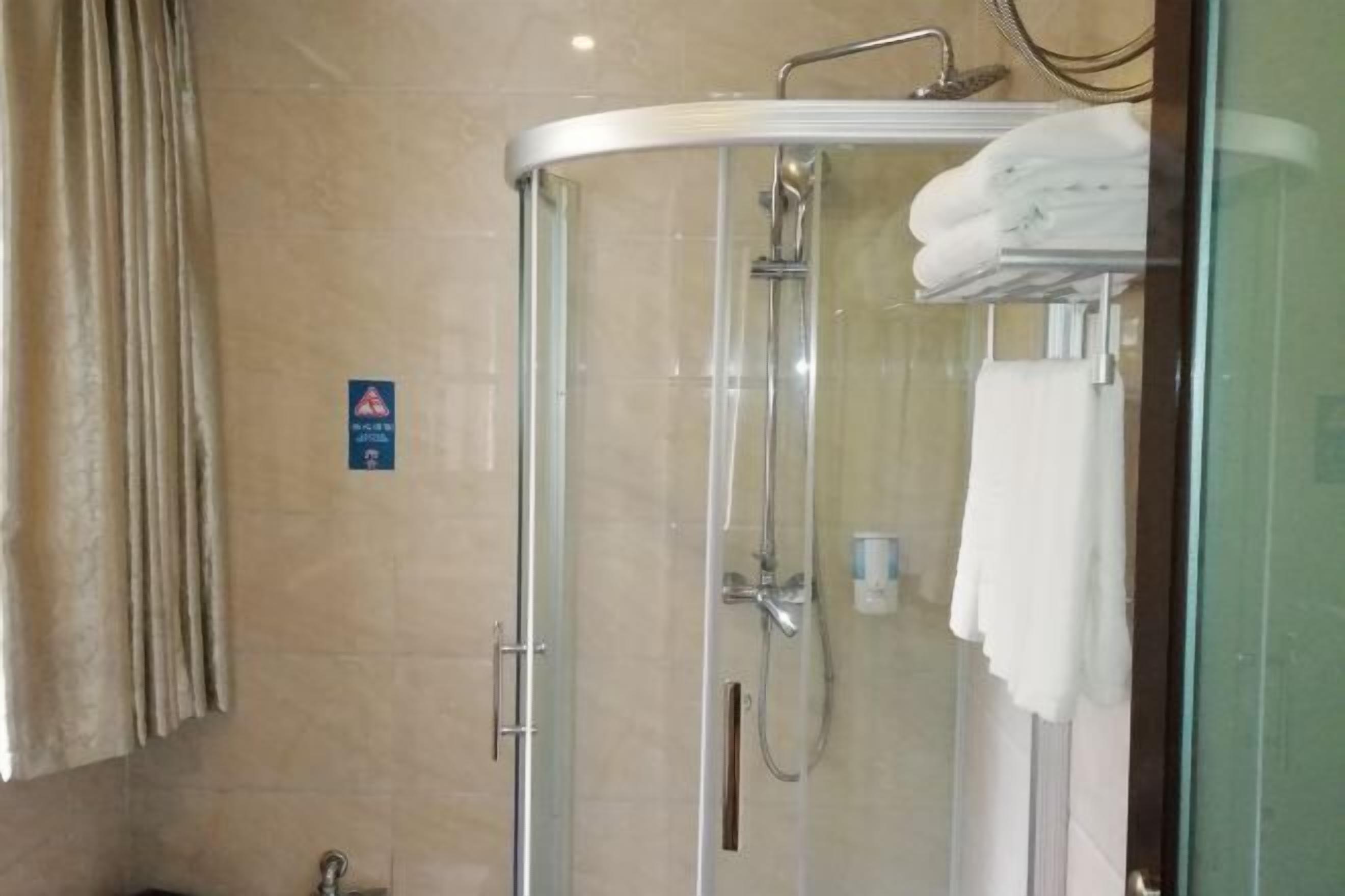 A glass-enclosed shower stall with a towel rack, a hand dryer, and a sign on the wall.