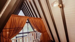 Et soveværelse med skråvæg, en seng med et orange pled og udsigt til en balkon.