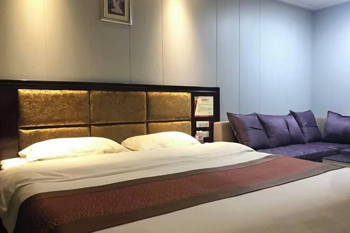 A hotel room with a bed, a sofa, a headboard, and a wall-mounted light fixture.