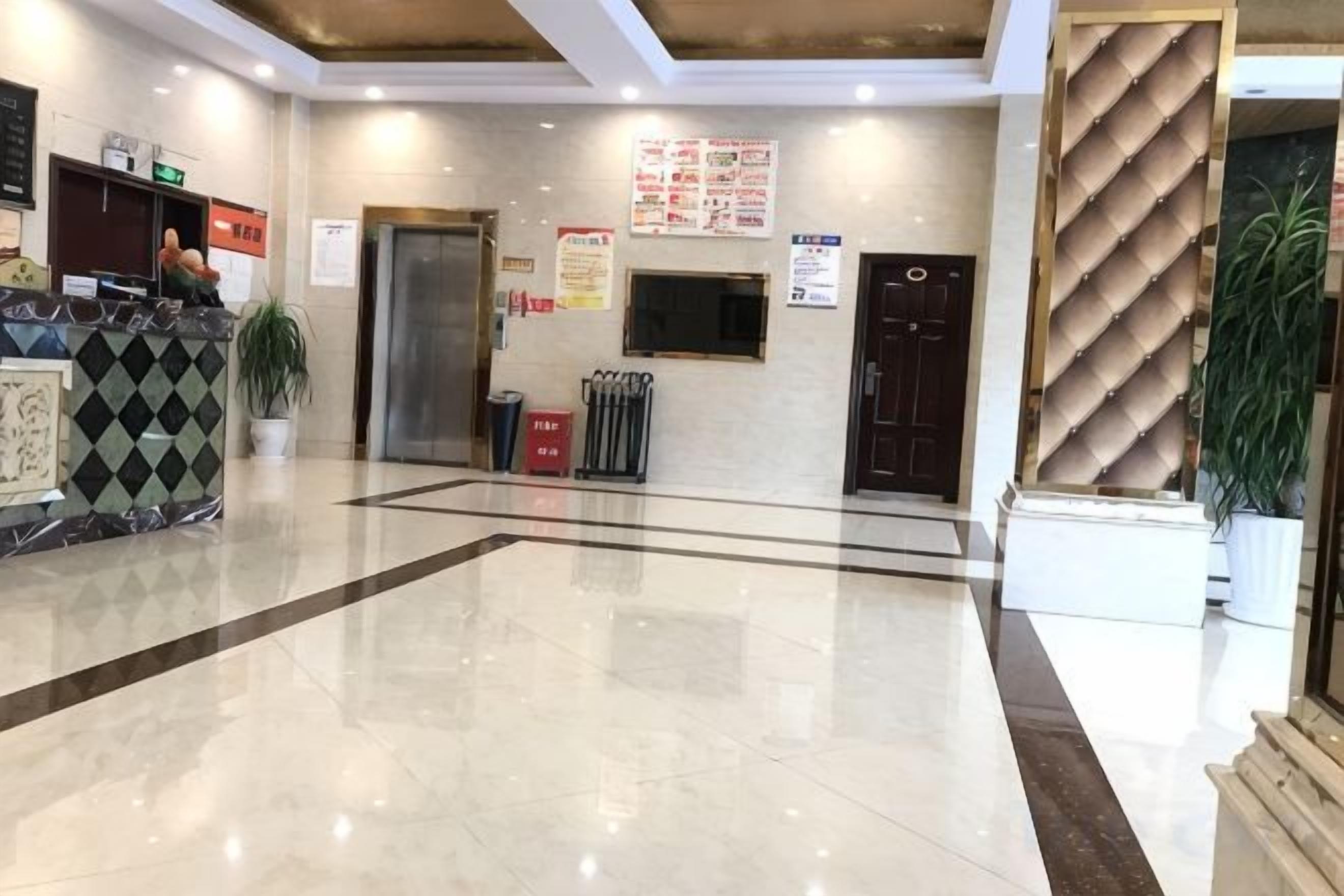 A hotel lobby with a reception desk, a plant, a trash bin, and a door.