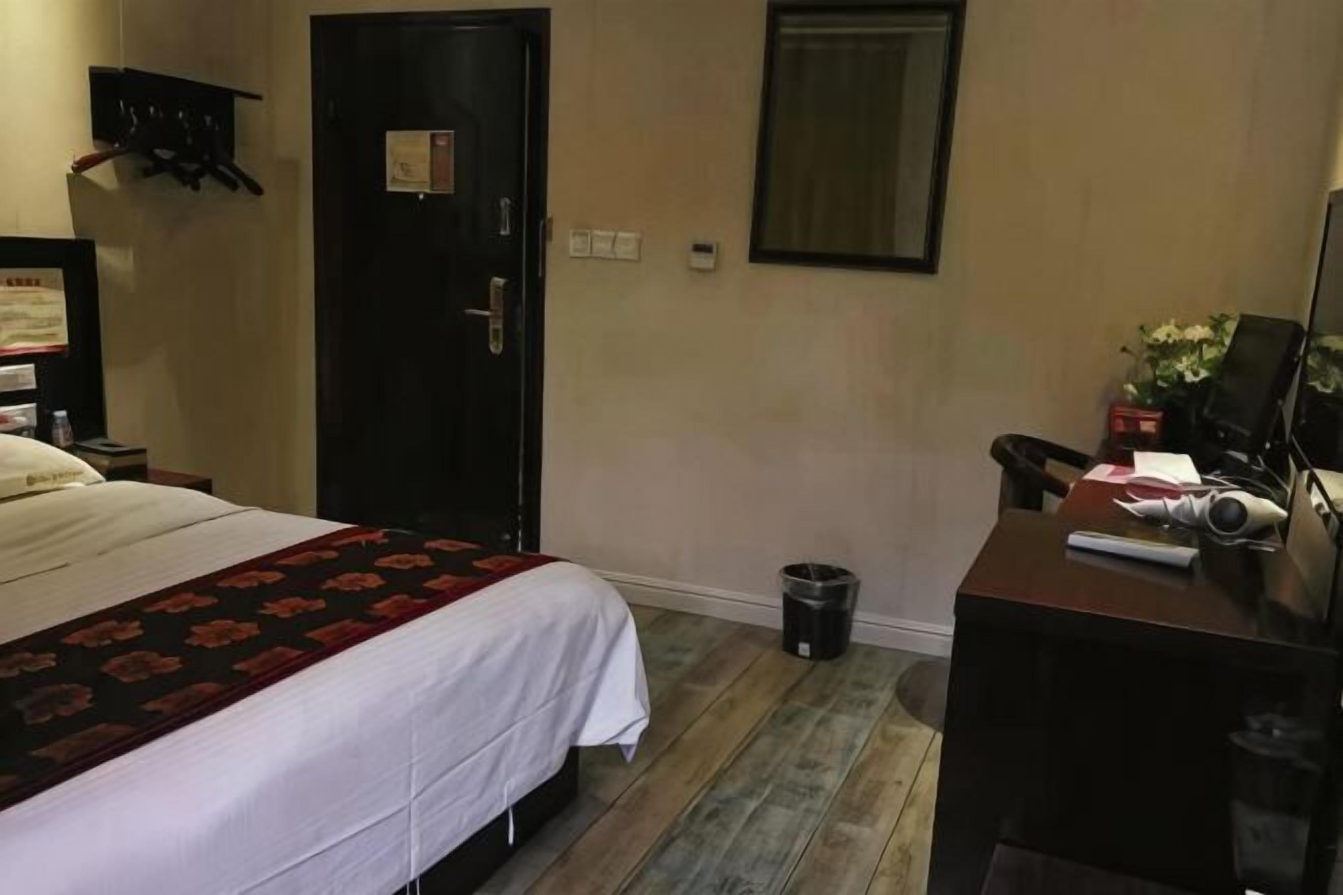 A hotel room with a bed, a desk, a chair, a trash bin, and a door.