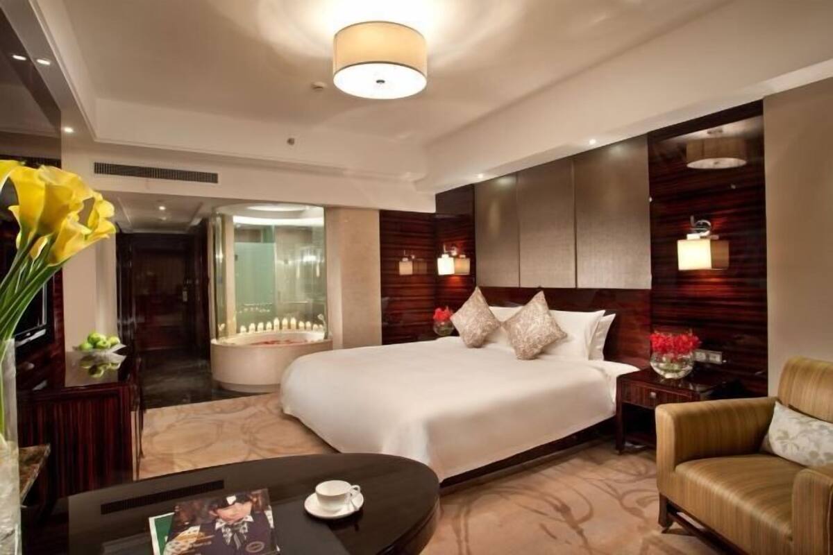 A modern hotel room with a large bed, a sitting area with a table, and a bathroom with a bathtub.