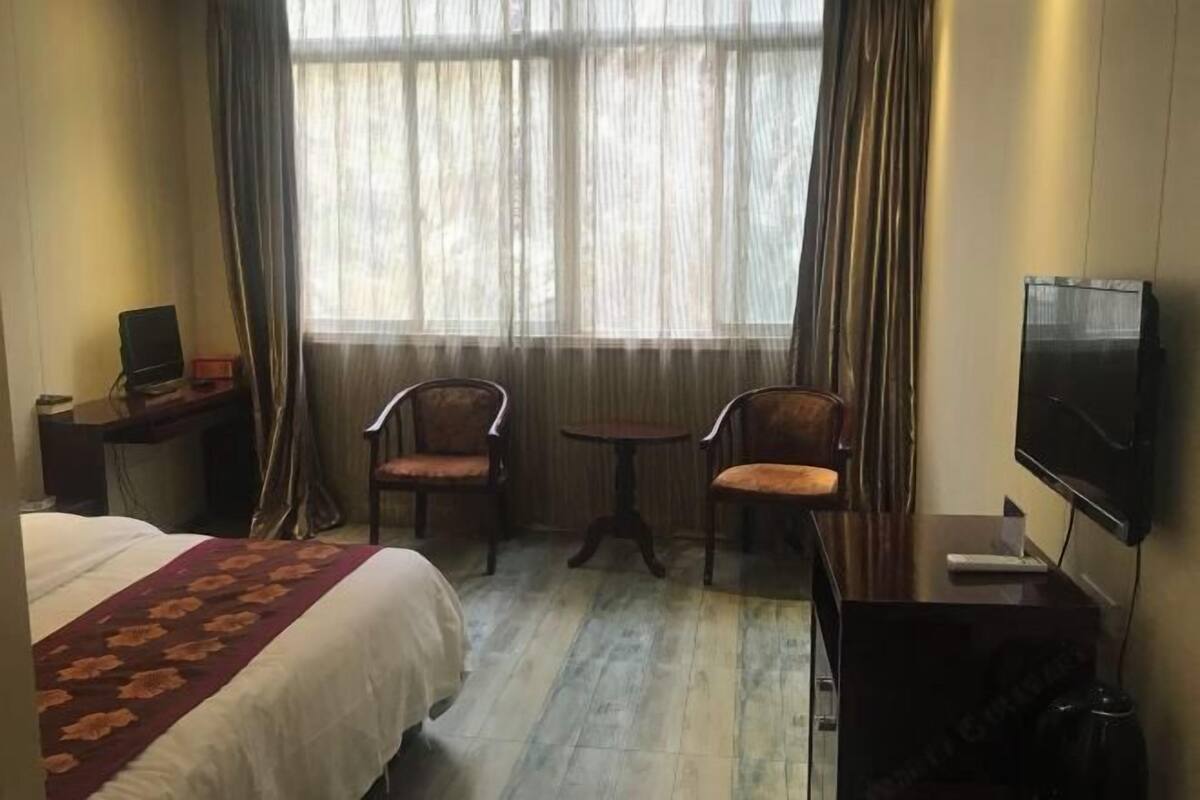 A hotel room with a bed, a desk with a computer, two chairs around a small table, and a TV on a stand.