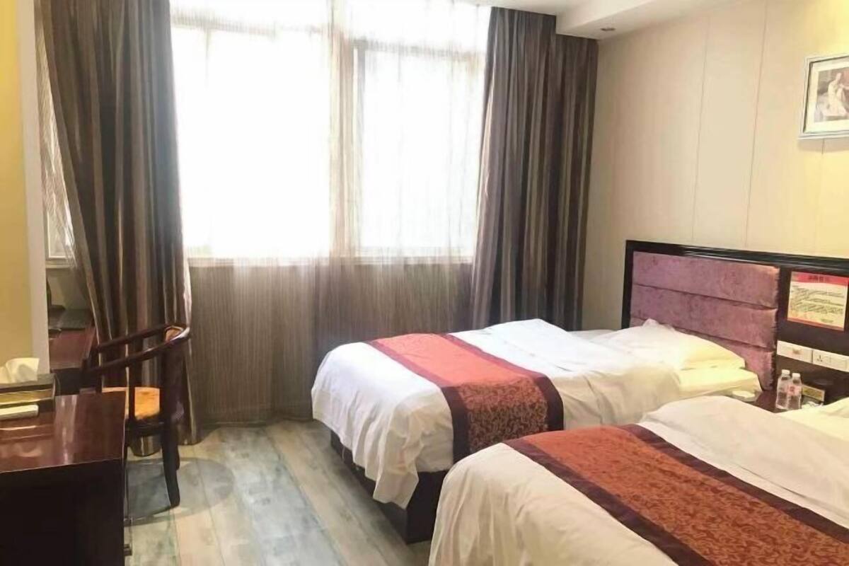 A hotel room with two beds, a desk, and a window with curtains.