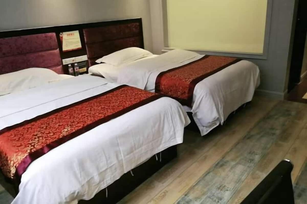 A hotel room with two beds, each with a red and white bedspread, a wooden headboard, and a window with blinds.