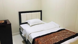 A neatly made bed with a white duvet and a patterned throw blanket, a dark wooden nightstand to the left, and a decorative wall panel above the bed. - Chongqing Hotel (Qinglong)