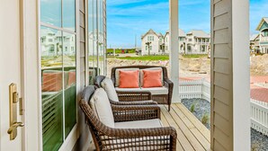 A balcony with wicker furniture and a view of coastal houses. - Brand-new townhome with porch, W/D, golf course, pool, & beach access (Port Aransas)