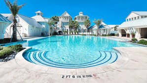 A large swimming pool with a 2 ft 6 in no diving depth marker, surrounded by white buildings with balconies and palm trees. - Brand-new townhome with porch, W/D, golf course, pool, & beach access (Port Aransas)
