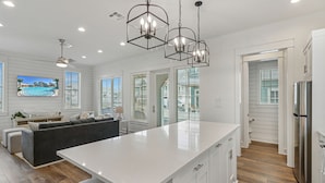 A modern kitchen with a large island, white cabinetry, and a stainless steel refrigerator. - Brand-new townhome with porch, W/D, golf course, pool, & beach access (Port Aransas)