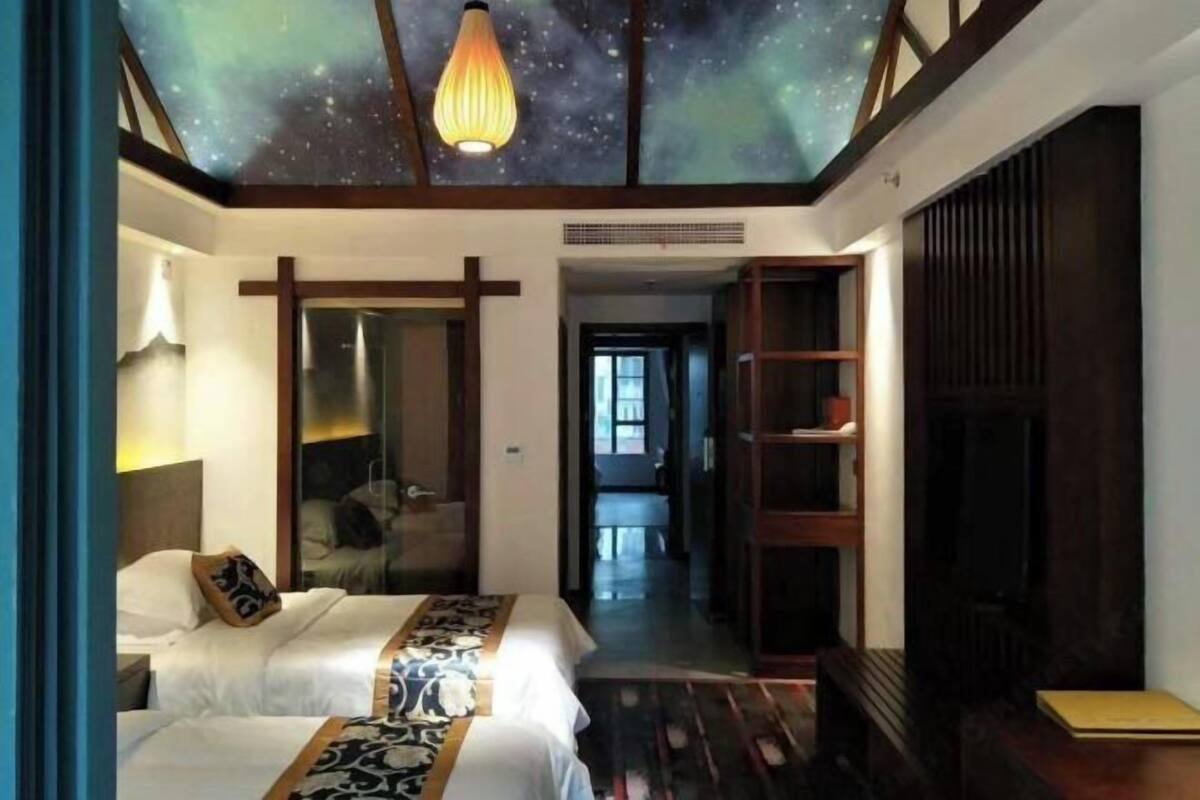 A hotel room with two beds, a starry ceiling, a wooden wardrobe, and a view into the hallway.
