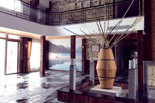 Un hall con un gran jarrón de madera como centro de atención, vista de un lago a través de un muro de cristal y una escalera de madera.