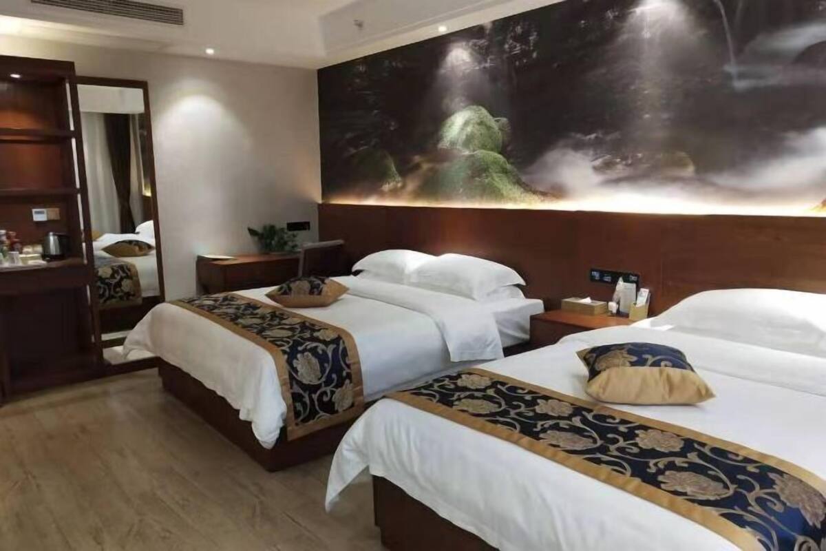 A hotel room with two beds, a large wall mural, a wooden nightstand, and a mirror.
