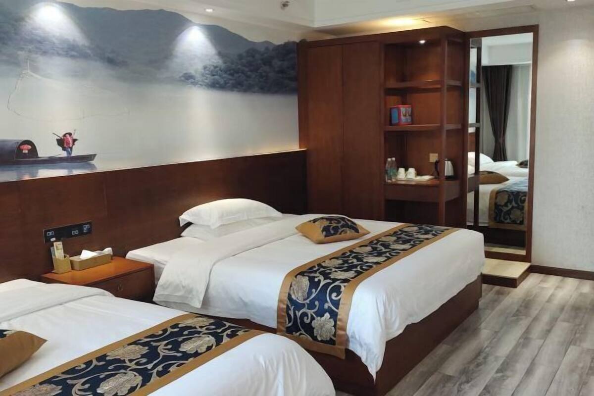 A hotel room with two beds, a wooden wardrobe, a nightstand, a mirror, and a mural on the wall.