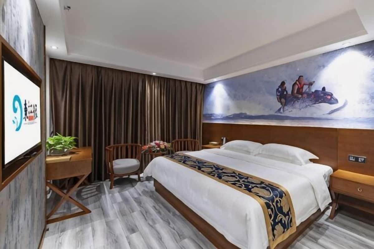 Habitación de hotel con cama, escritorio, silla, televisor y un cuadro en la pared.
