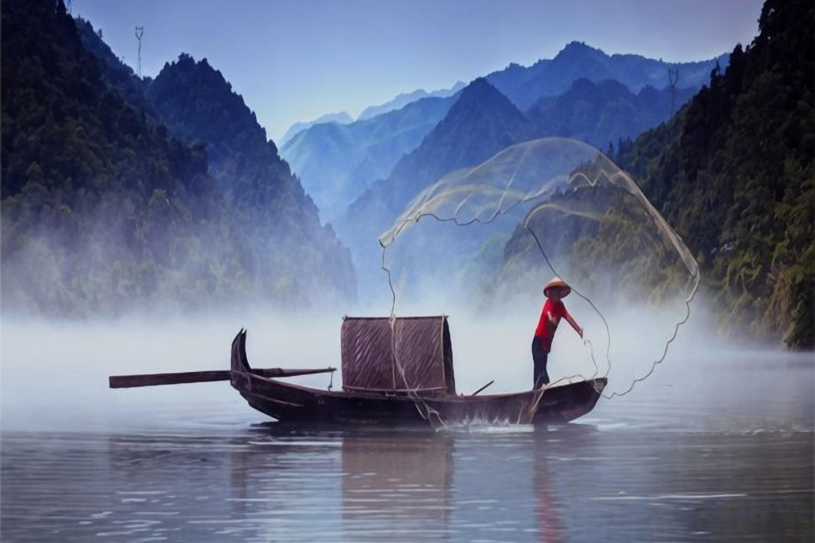 A person in a boat with a net, surrounded by misty mountains.