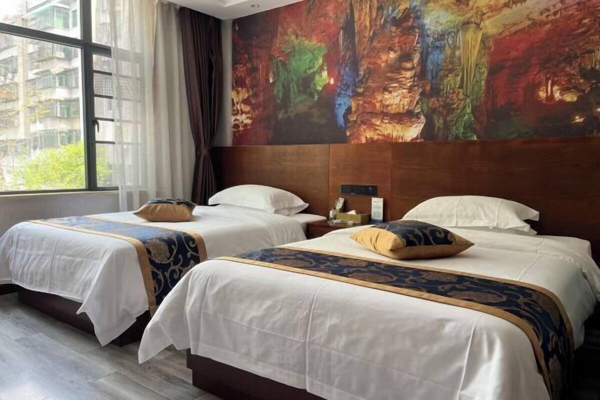 A hotel room with two beds, a large window, and a colorful mural on the wall.