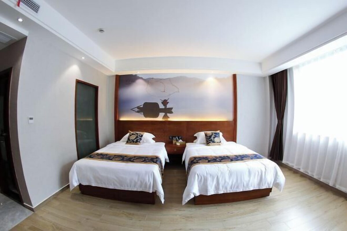 A hotel room with two beds, a large wall mural, and a window with curtains.