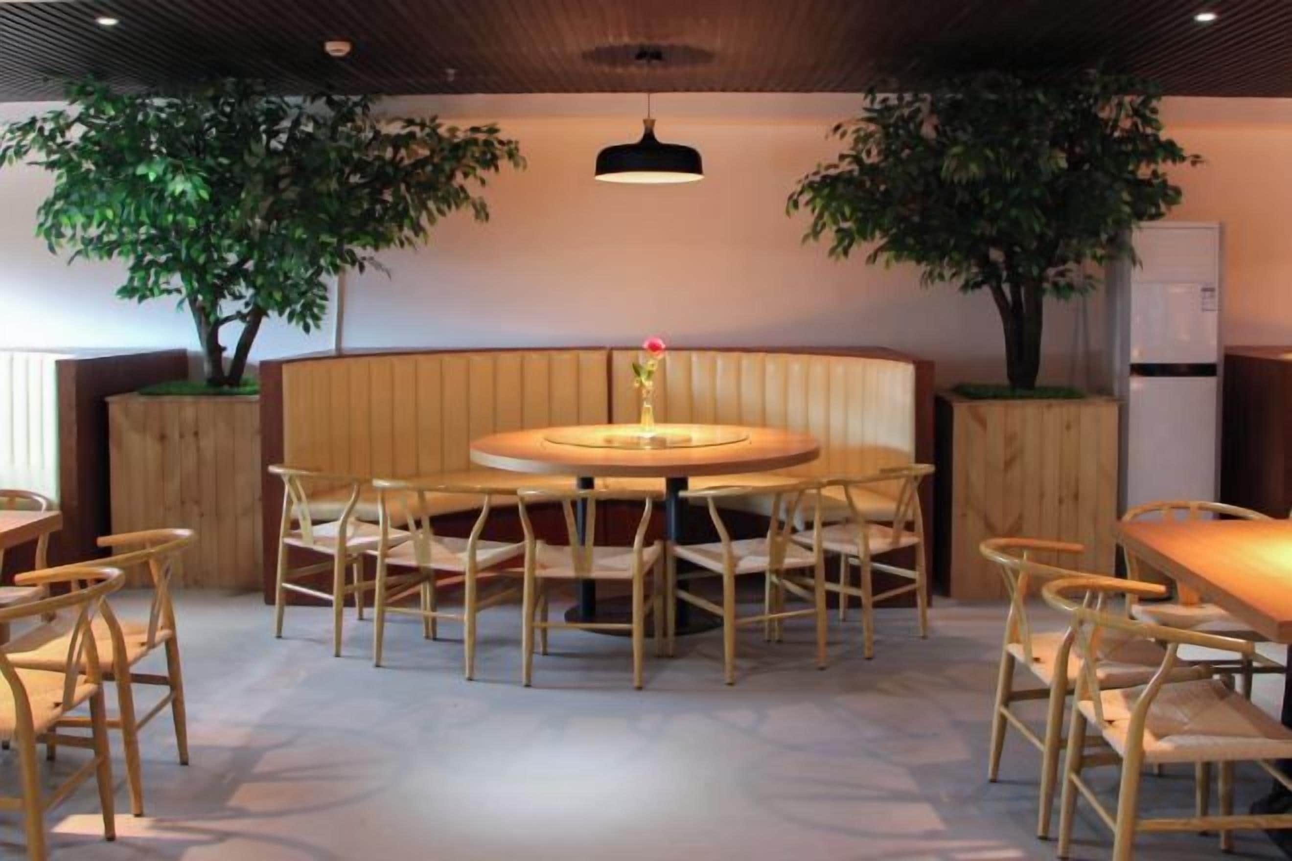 Un comedor con una mesa redonda rodeada de sillas, un banco de madera y dos macetas.