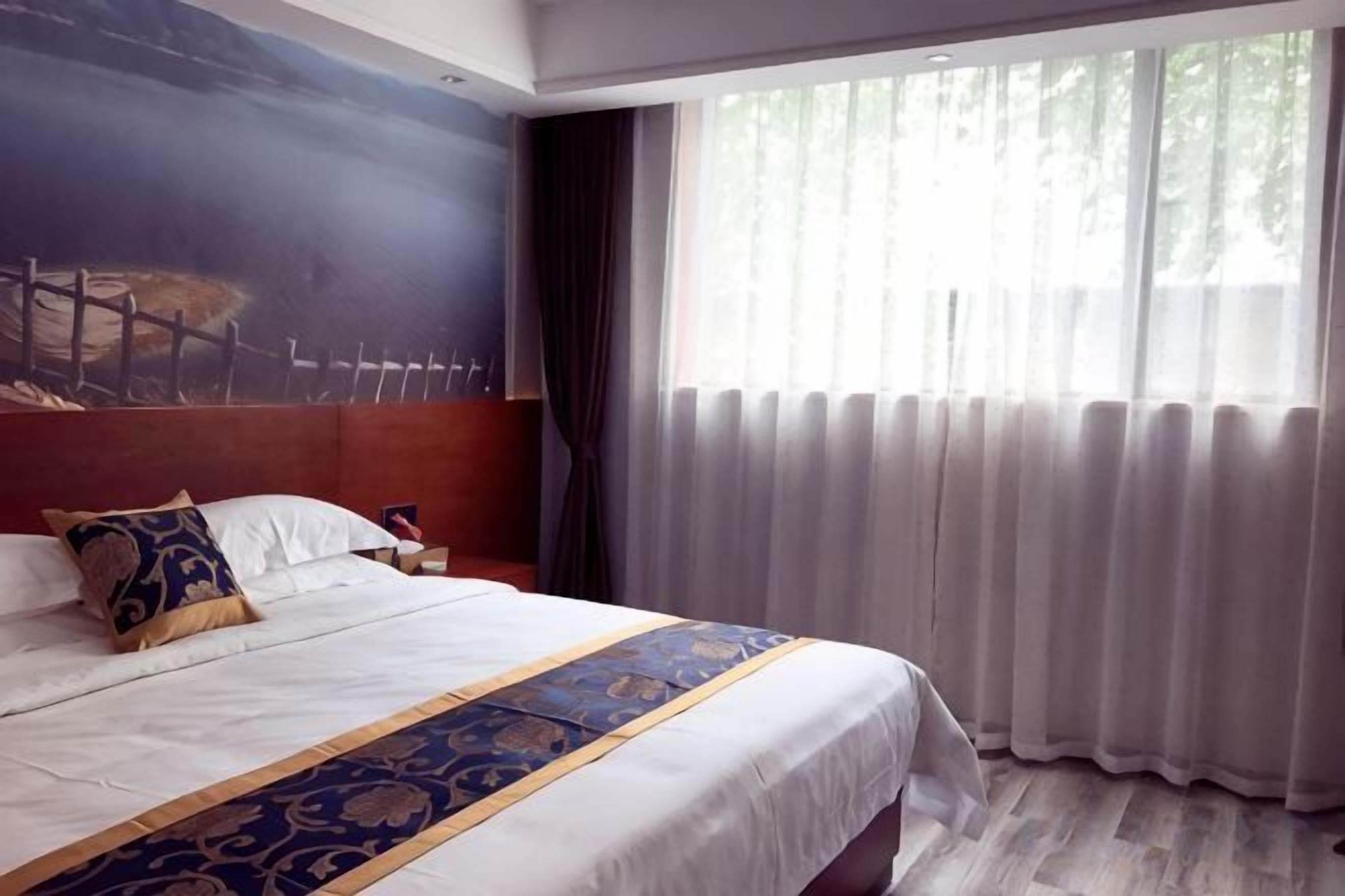 Habitación de hotel con una cama grande, una mesita de noche, un cuadro en la pared y una ventana con cortinas.