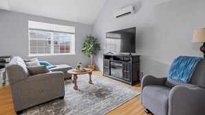 A living room with a grey sofa, a coffee table, a TV, and a plant. - Harbourview Loft B Two Bedroom Loft Apartment Located in Downtown Summerside (Summerside)