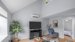 A modern living room with a flat-screen TV, a fireplace, a grey sofa, a small round coffee table, and a potted plant. - Harbourview Loft B Two Bedroom Loft Apartment Located in Downtown Summerside (Summerside)
