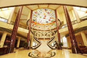 A grand hotel lobby with a central staircase, marble columns, and a large decorative ceiling. - Dongfang Hotel (Rushan)