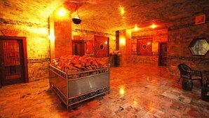 Um quarto com parede de pedra, cama com estrutura de metal e um banco.