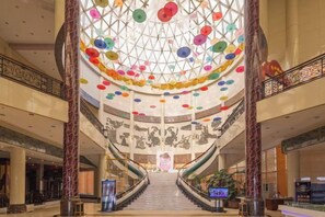 A grand atrium with a central staircase, a glass ceiling with colorful circular decorations, and a large mural on the walls. - Dongfang Hotel (Rushan)